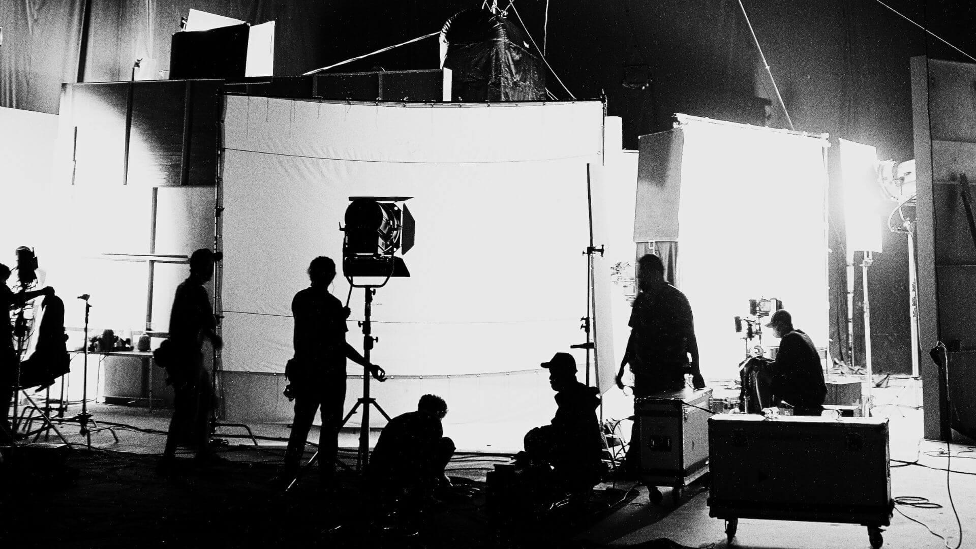 Film Set Production & Soundstage Workflows — Jessica Evelyn Rodrigues de Lima Wide black and white shot of a film soundstage with studio lighting setups and the production crew actively working on set.