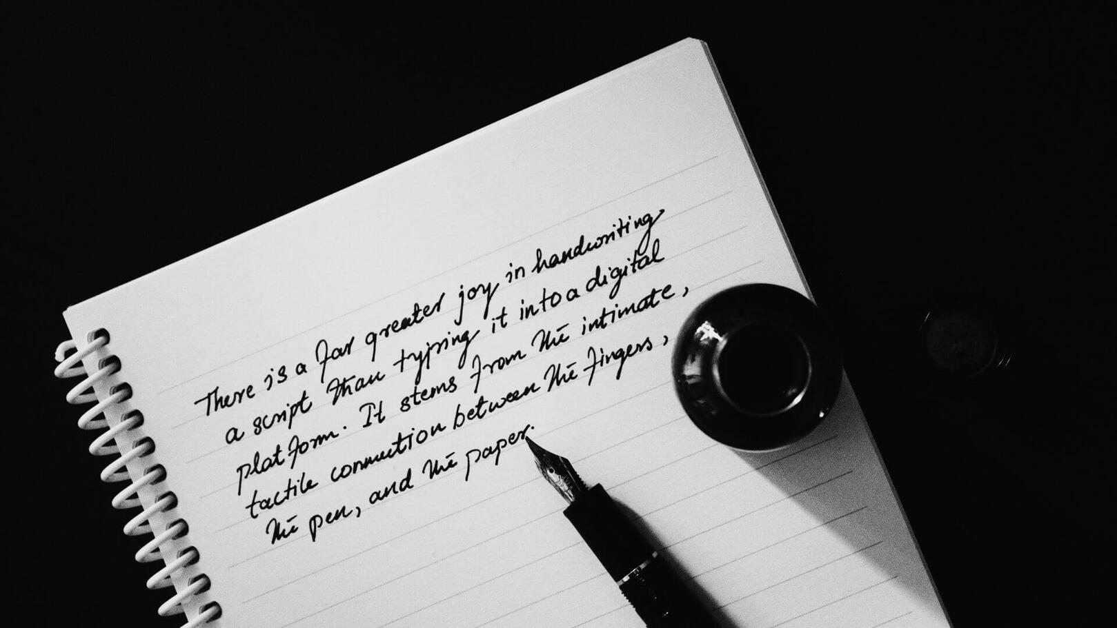 Storytelling & Screenwriting — Creative Process | Jessica Evelyn Rodrigues de Lima Top-down view of a notebook with handwritten text, a fountain pen, and an ink bottle on a workspace.