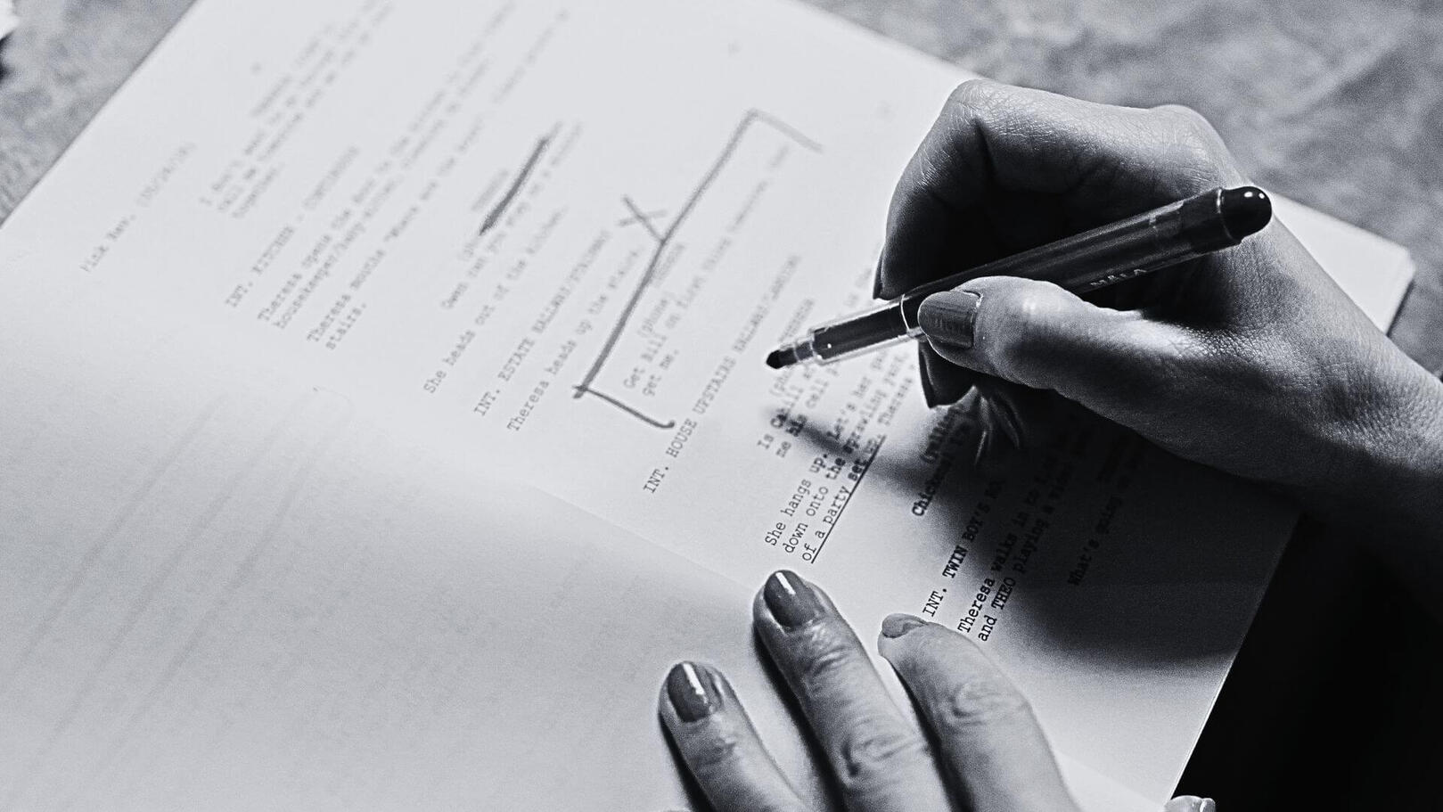 Narrative Consulting & Script Editorial — Jessica Evelyn Rodrigues de Lima Black and white detail shot of a hand highlighting and annotating revisions with a pen on a printed screenplay page.